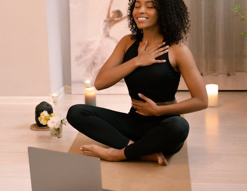 African American woman practicing yoga and meditation indoors with a laptop.