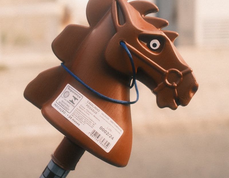 Close-up of a brown toy horse head on a stick outdoors.