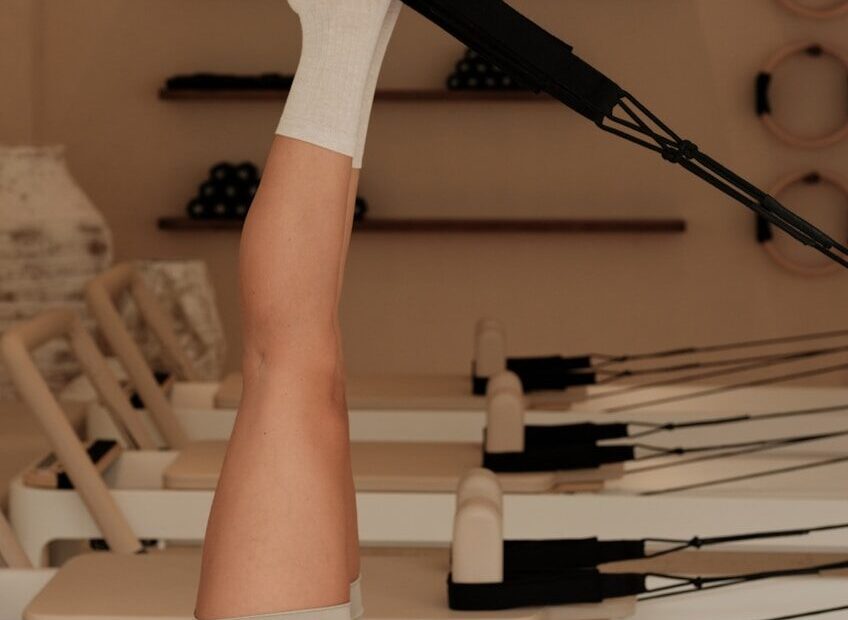 Woman does pilates exercise on a reformer machine.